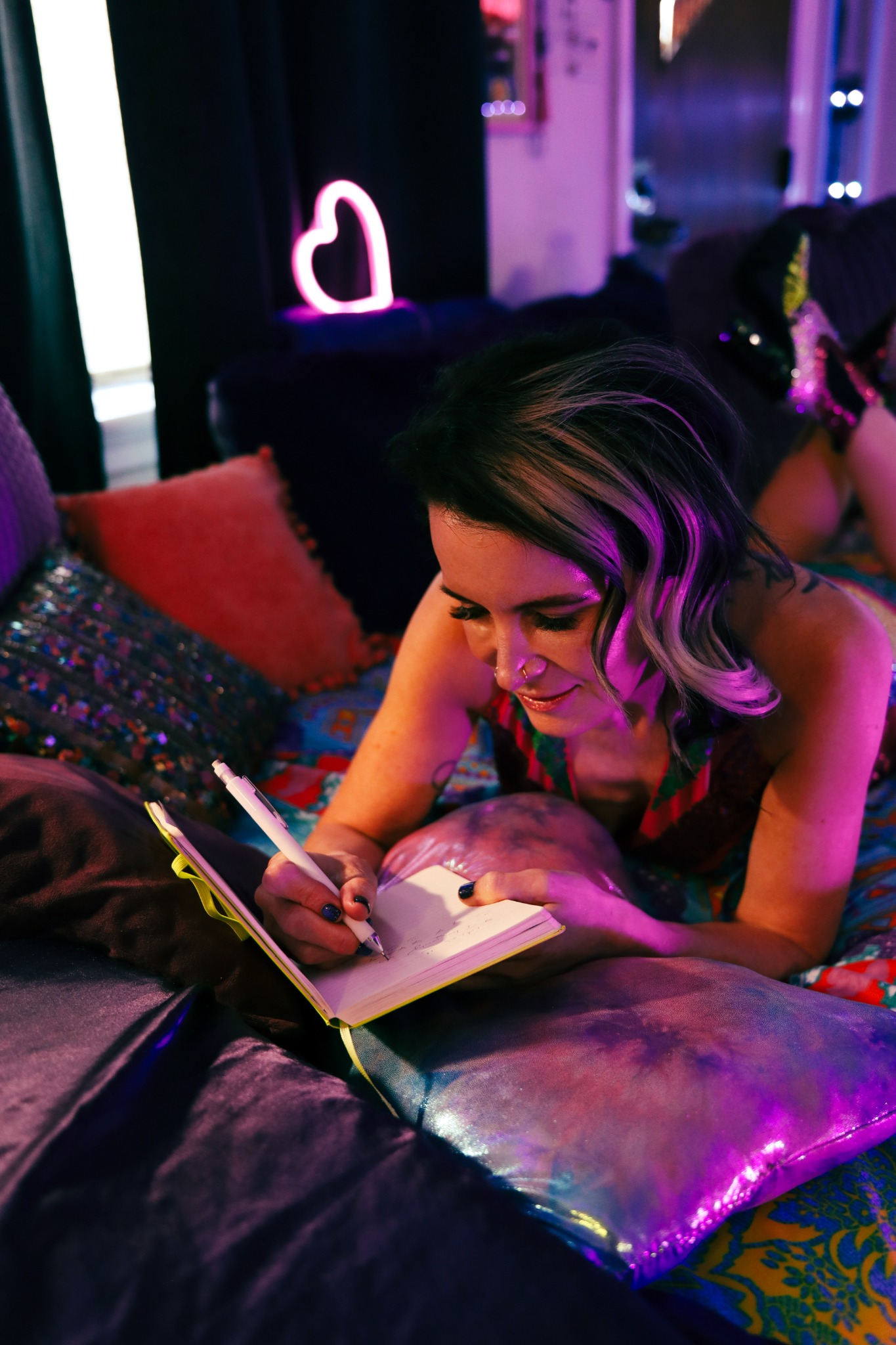 Jerene writing in a notebook in a colorful, neon-lit room